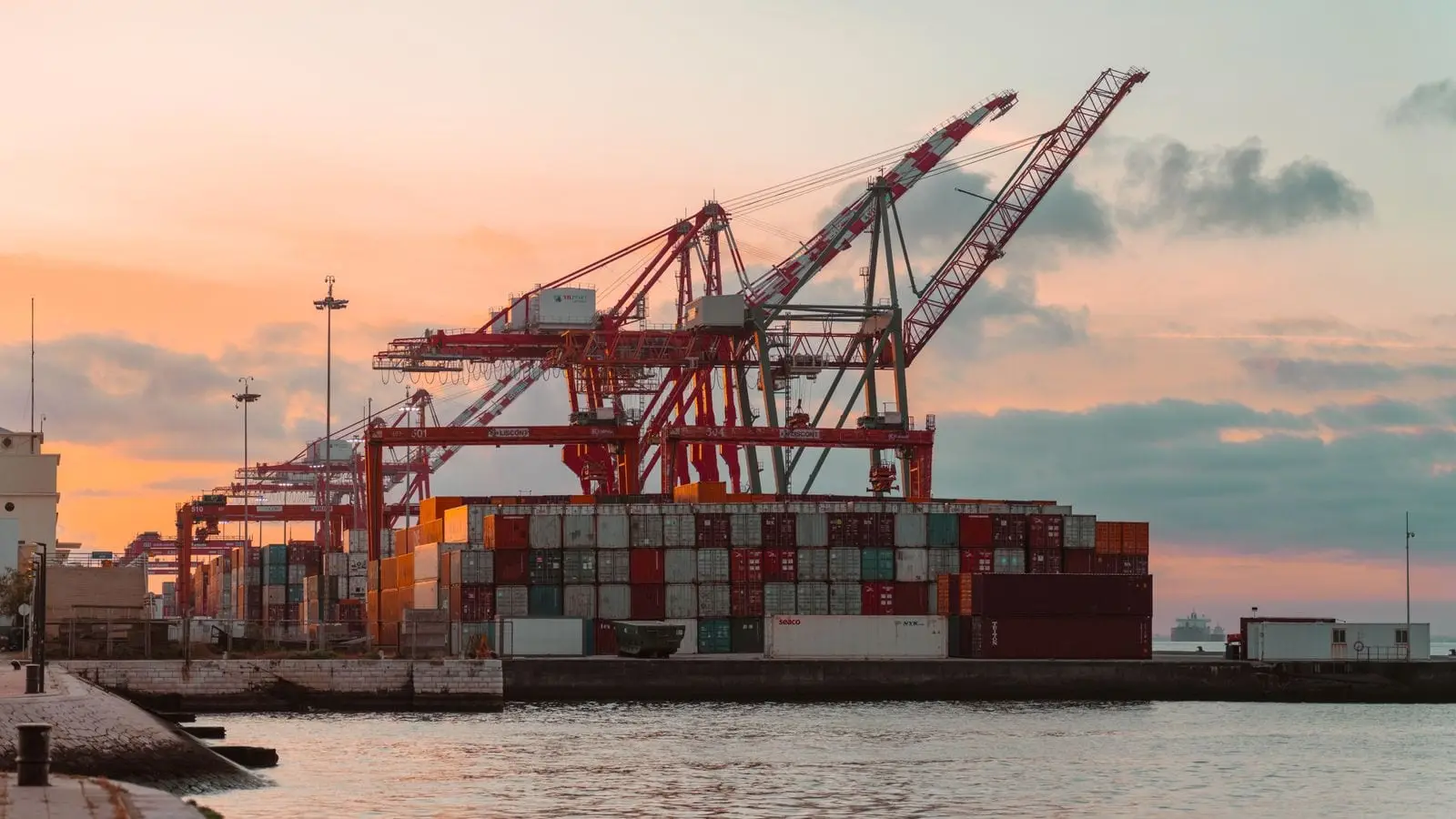 Container cranes loading a cargo vessel at a terminal during sunset